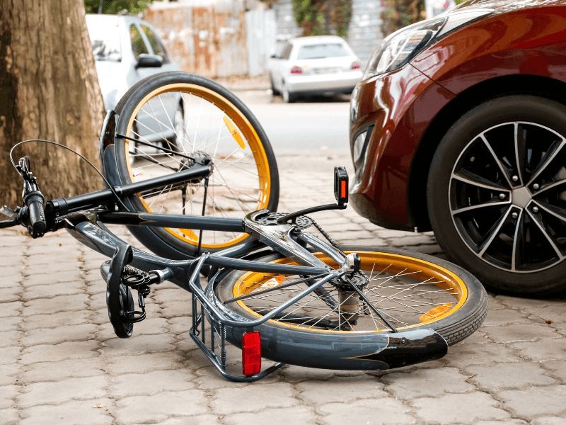 bicycle on its side next to a car on cobblestone roadway
