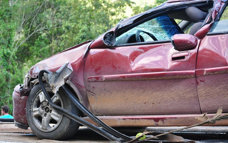 A red car severely damaged from a crash, with crumpled metal and shattered glass visible on the front and side.