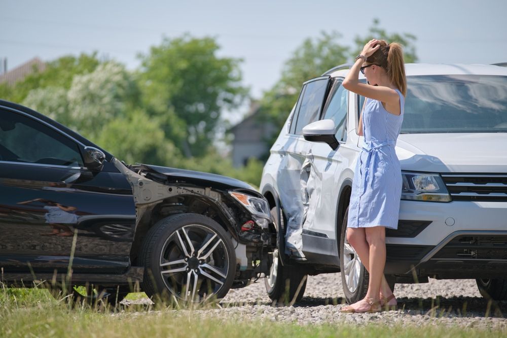 Una mujer angustiada, con la cabeza entre las manos, se encuentra entre un coche negro accidentado y un todoterreno blanco abollado tras un choque.