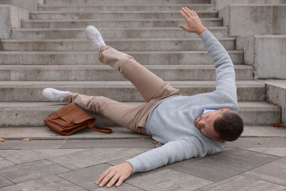 Man falling backward on outdoor concrete steps with his bag beside him after slipping