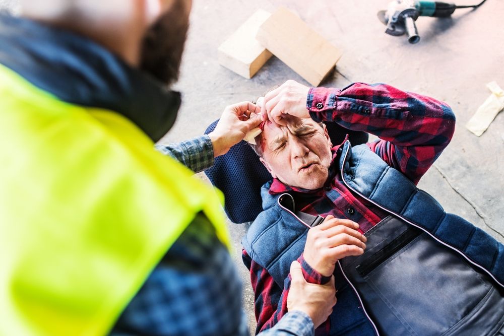 Un compañero de trabajo, que lleva un chaleco de seguridad, atiende la herida sangrante en la cabeza de un trabajador lesionado en una obra.
