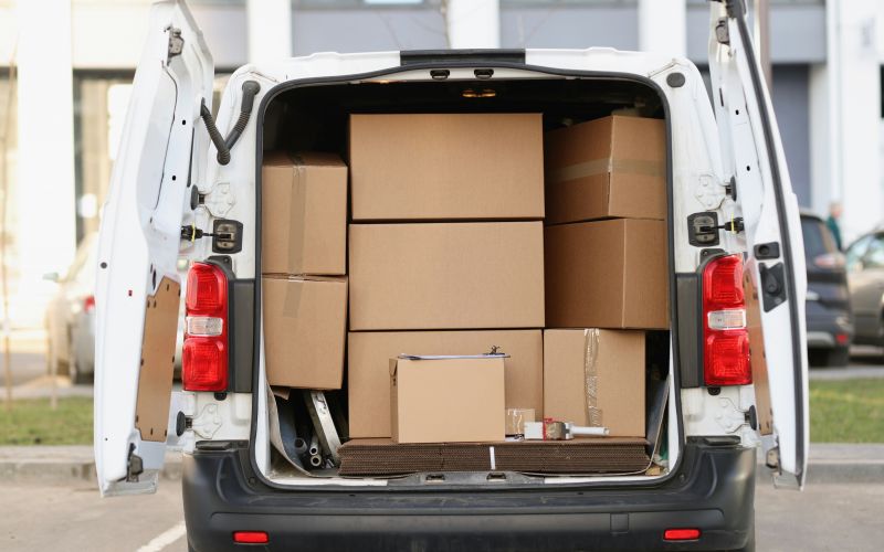 A delivery van with its rear doors open, showing a tightly packed load of cardboard boxes stacked inside.