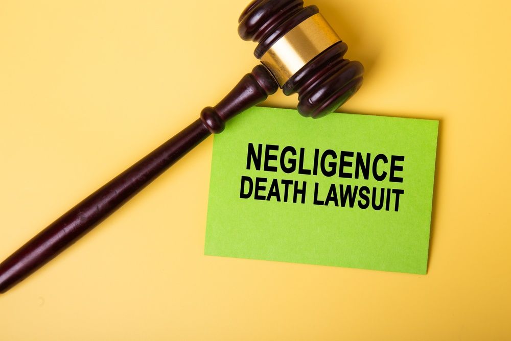 Un mazo judicial junto a una tarjeta de color verde neón en la que se lee «DEMANDA POR MUERTE POR NEGLIGENCIA», sobre un fondo amarillo.