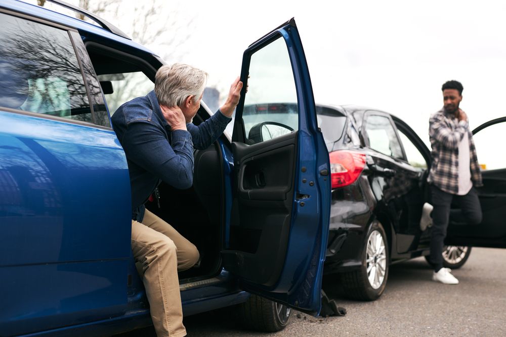 Two drivers holding their necks in pain as they exit their vehicles after a rear-end collision