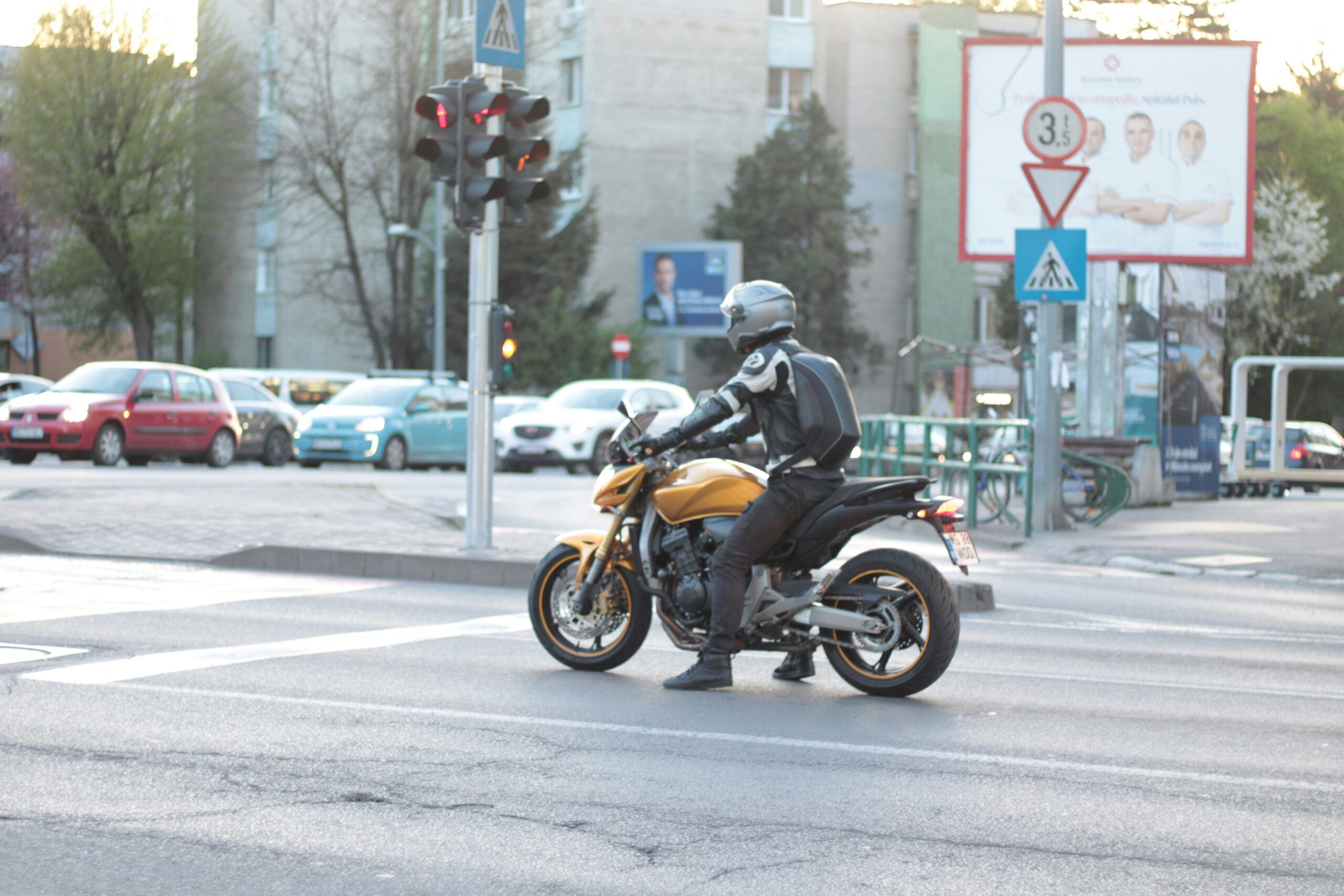 A motorcyclist in full protective gear waiting at a red light on a yellow sport bike in a busy urban intersection.