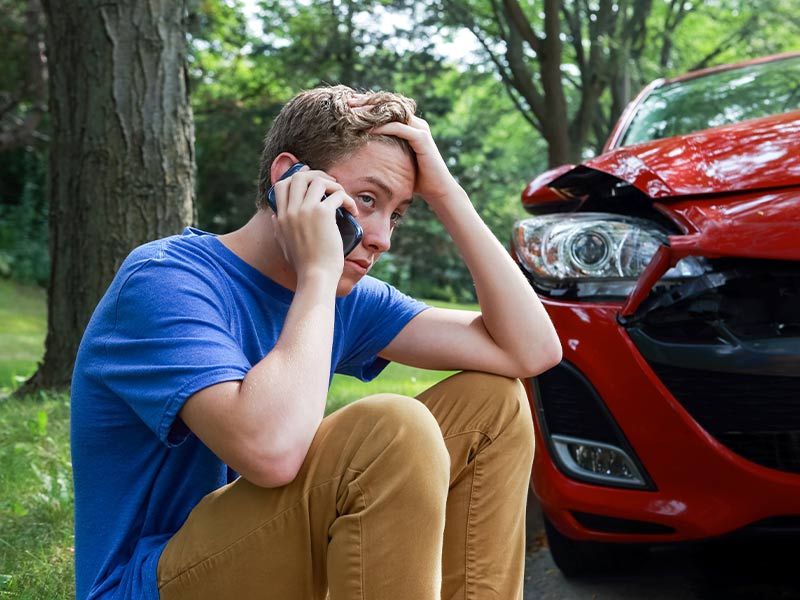 young male sitting outside a car accident on his phone