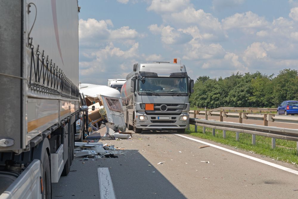 Debris scattered across a highway after a semi-truck collided with a caravan trailer between two large trucks.