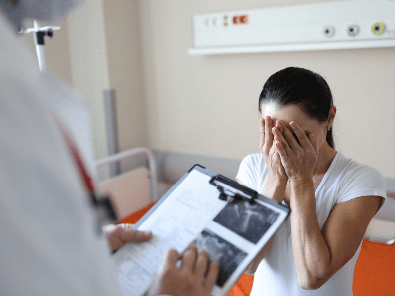 Doctor speaking to a woman who is holding her face in her hands
