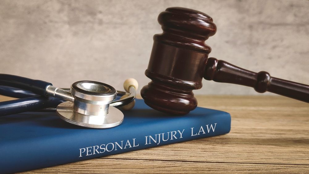 A gavel and stethoscope rest on a blue book titled "Personal Injury Law" on a wooden table.