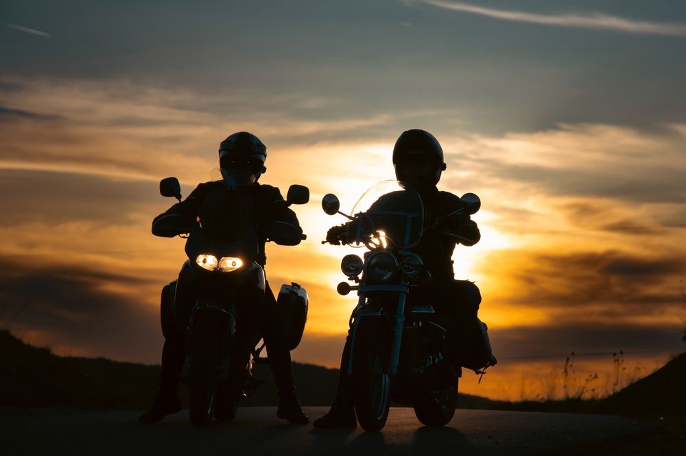 Two motorcyclists in helmets stopped side by side on a road at sunset