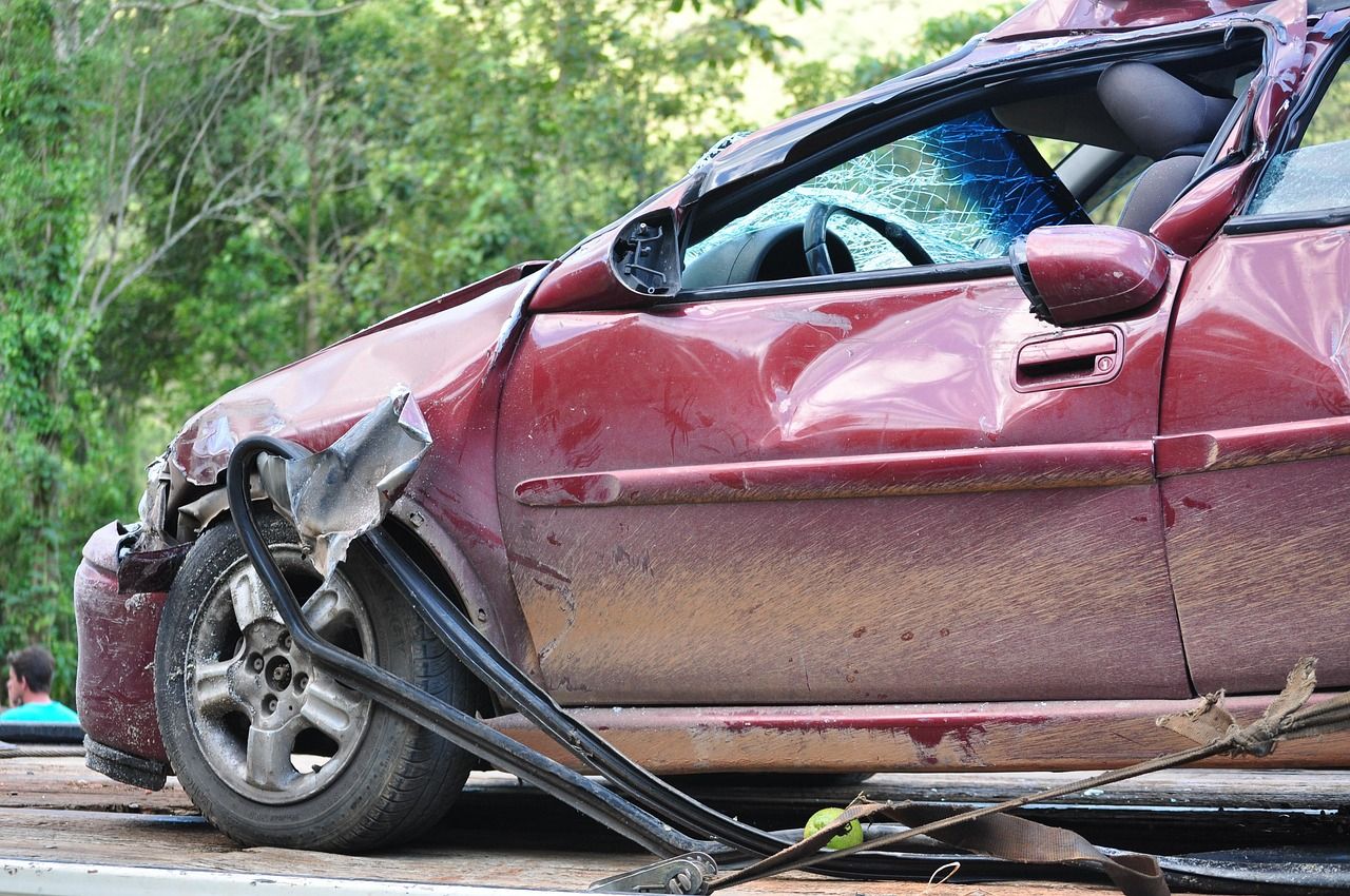 A red car severely damaged from a crash, with crumpled metal and shattered glass visible on the front and side.