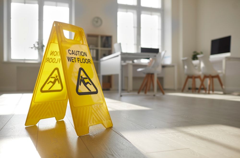 Yellow "Caution: Wet Floor" sign standing on a hardwood floor with sunlight streaming across it.