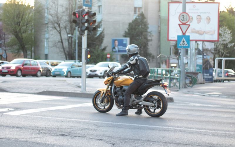 A motorcyclist in full protective gear waiting at a red light on a yellow sport bike in a busy urban intersection.