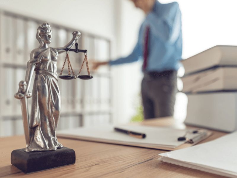 Man on phone in background with justice scales on desk in foreground