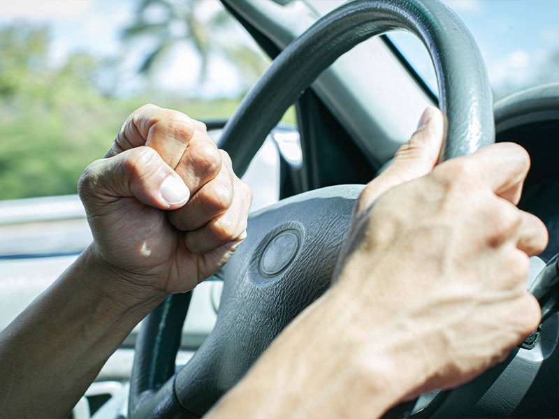 man angrily hitting his steering wheel