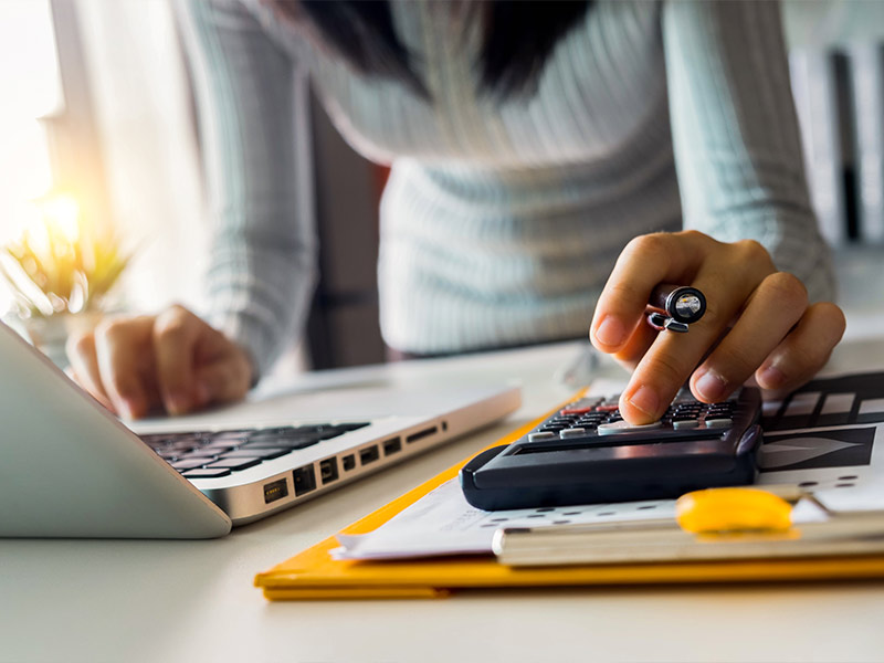 A woman using a calculator next to a computer