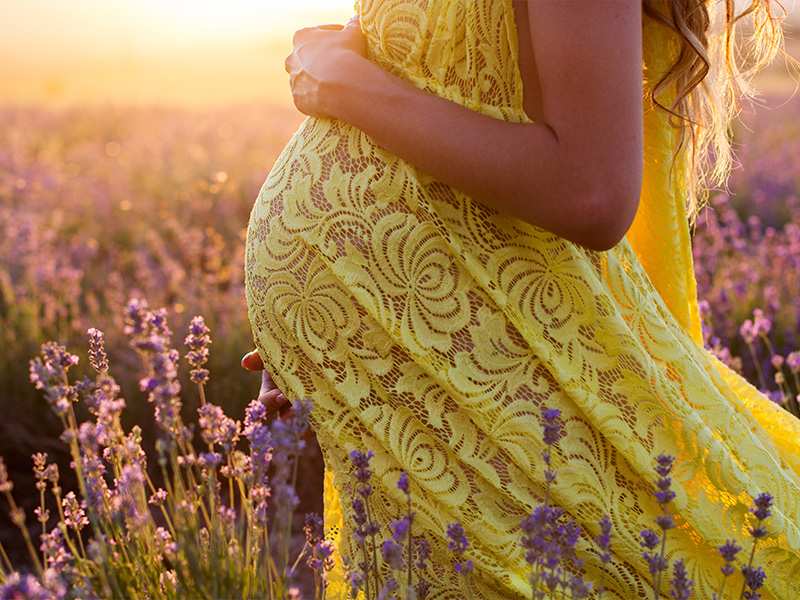 a pregnant woman standing in a field holding her stomach