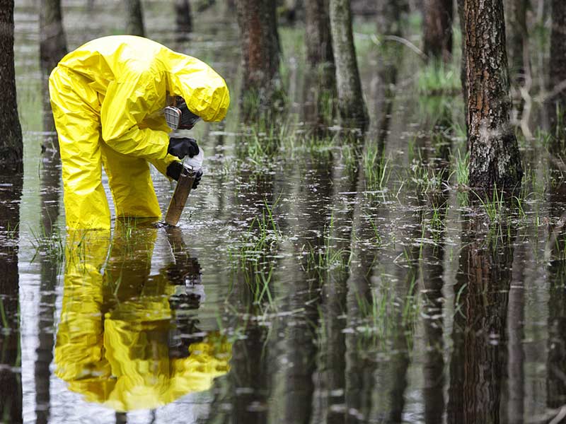 man wearing a hazmat suit collecting water samples from a river