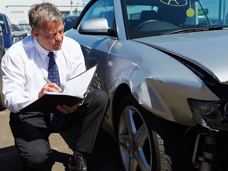 An insurance adjuster looking at a car with front end damage