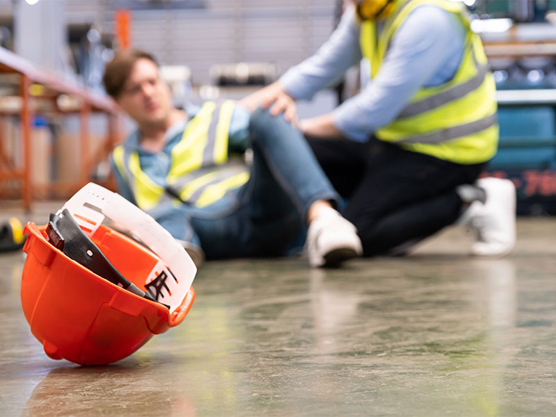 injured warehouse worker laying on the floor being helped up by another employee