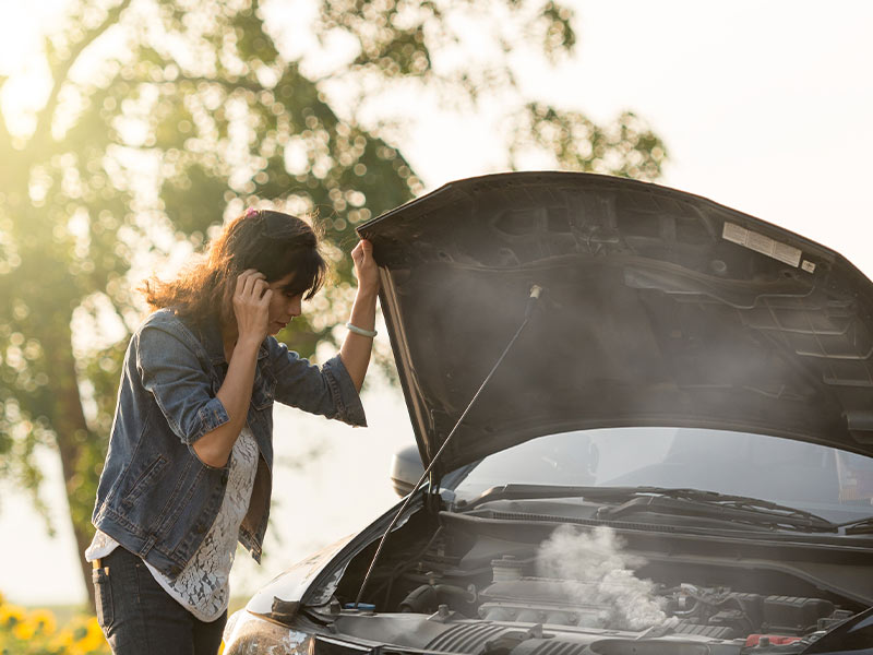 woman looking at the smoking engine of her car