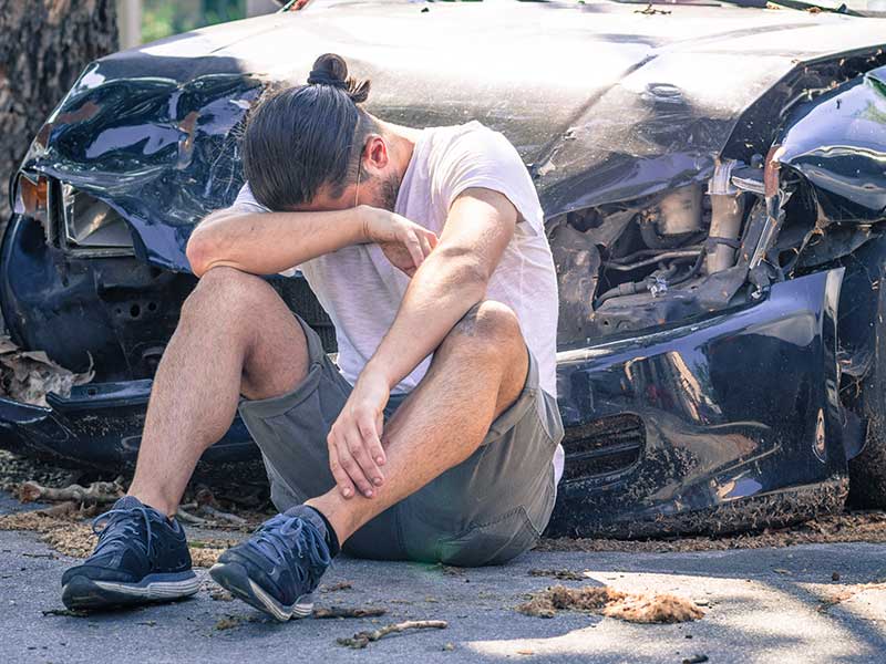 man sitting in front of a car accident crying