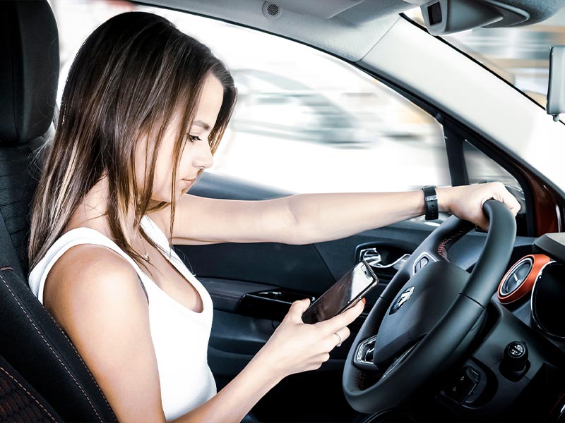 young woman looking at her phone while driving her car