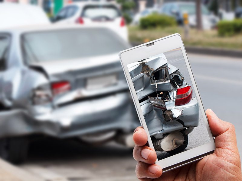 man taking a picture of the rear end damage to his car