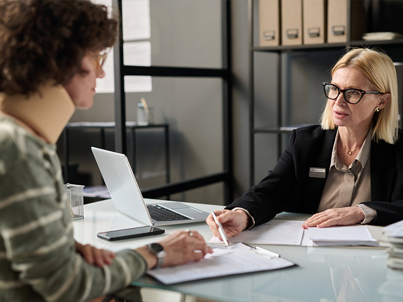 female attorney sitting down and talking with a woman wearing a neck brace