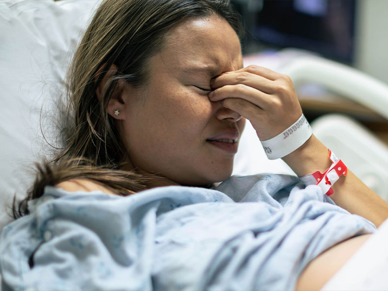 woman laying in a hospital bed holding her head in pain