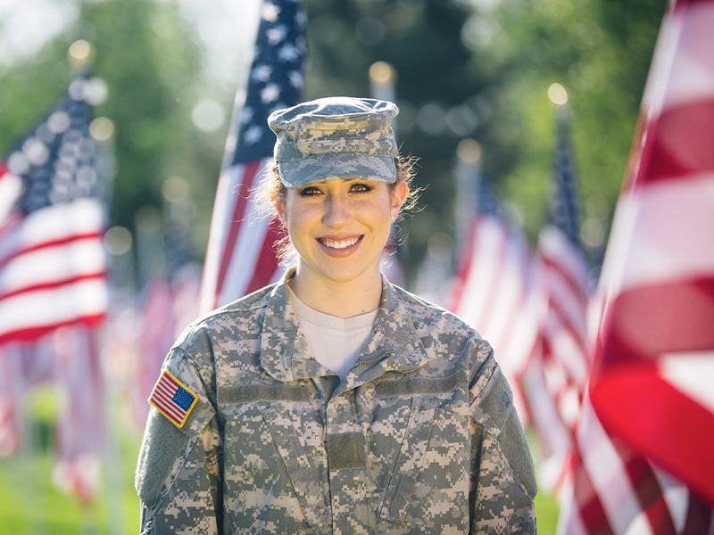 female soldier standing in front of the United States flag smiling