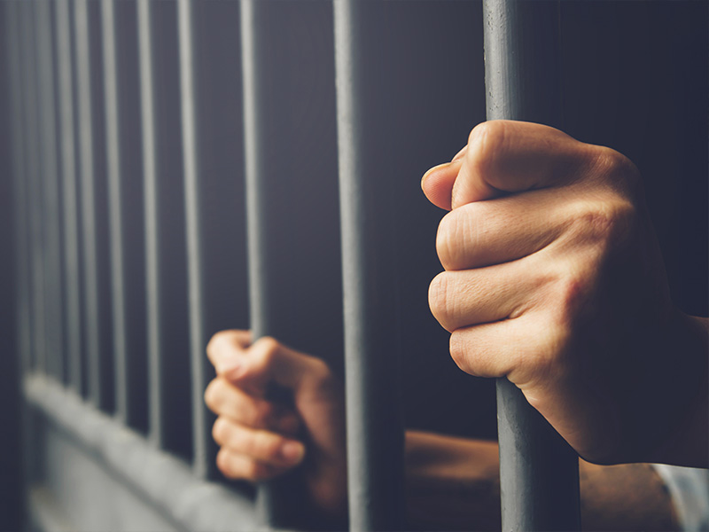 man inside a jail cell holding onto the bars