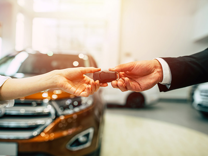 car salesman handing the keys to a car to a woman