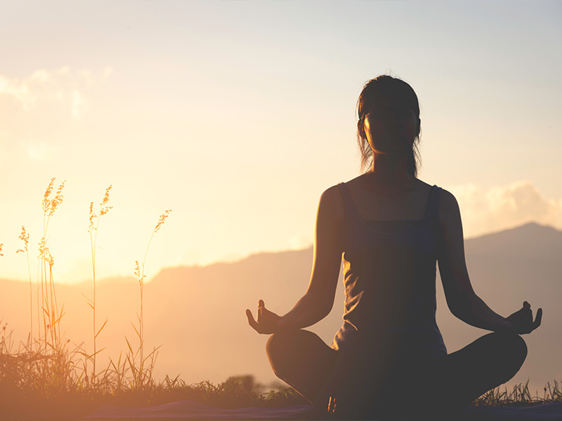 a woman meditating at sunset