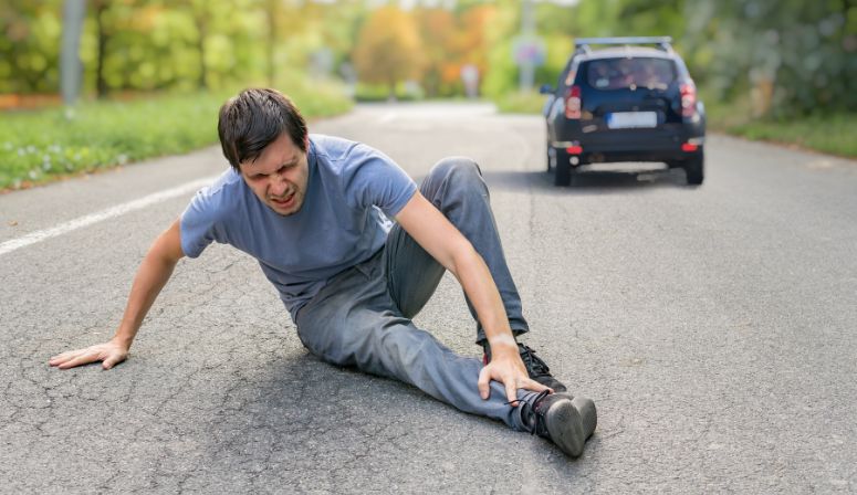 car driving past man laying in road