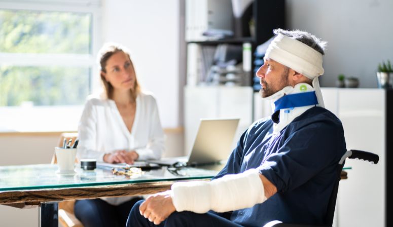 man in wheelchair next to desk speaking to a lawyer about a personal injury claim.