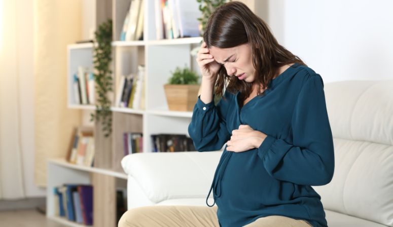 woman sitting on couch holding head and stomach