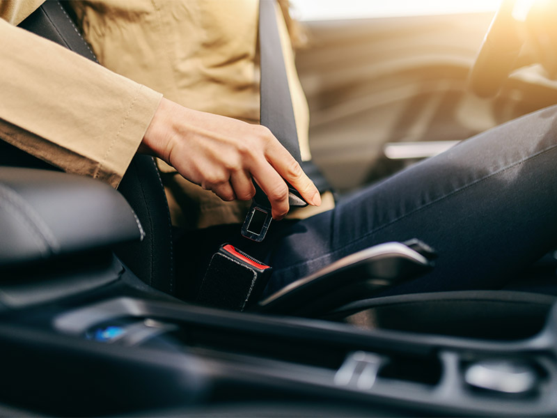 woman sitting in her car putting on a seatbelt