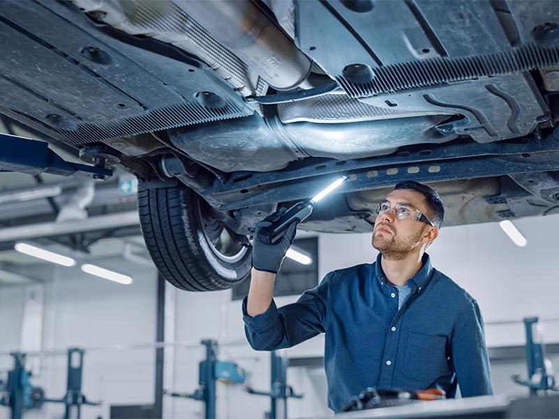 mechanic looking at the undercarriage of a car
