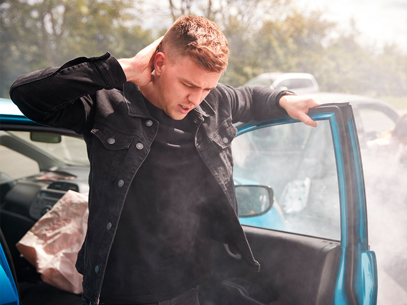 man holding his neck exiting his car after an auto accident 