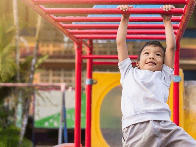 young boy playing on playground using monkey bars