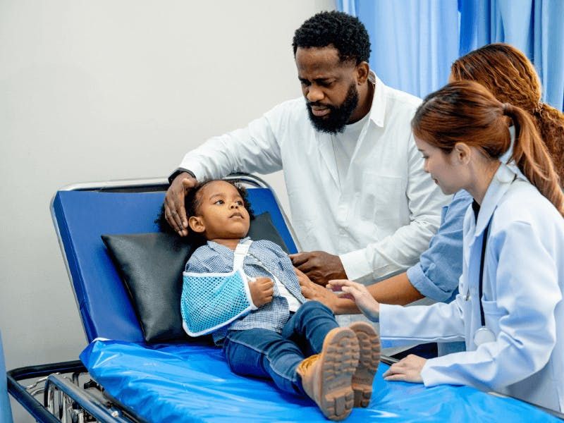 father consoling child laying in hospital bed with broken arm