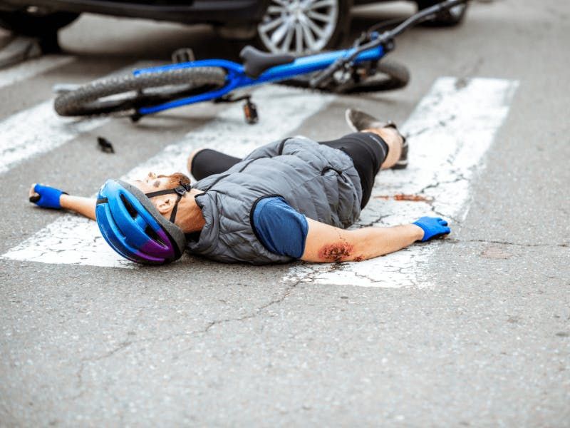 injured man on ground next to his bike in front of vehicle on roadway