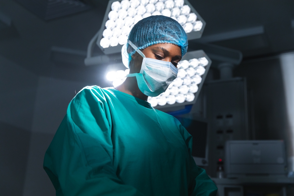 A woman in a surgical suit stands in a dimly lit environment, conveying a sense of seriousness and focus.
