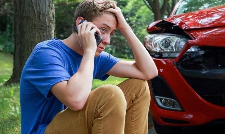 a teenager on his phone in front of a car accident