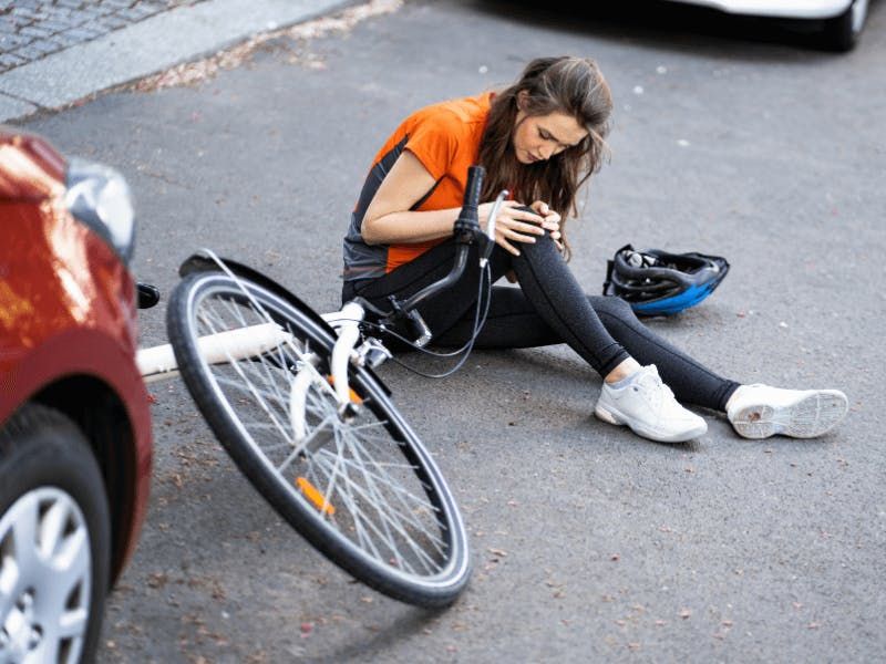 woman checking her knee on ground with bike in front of car