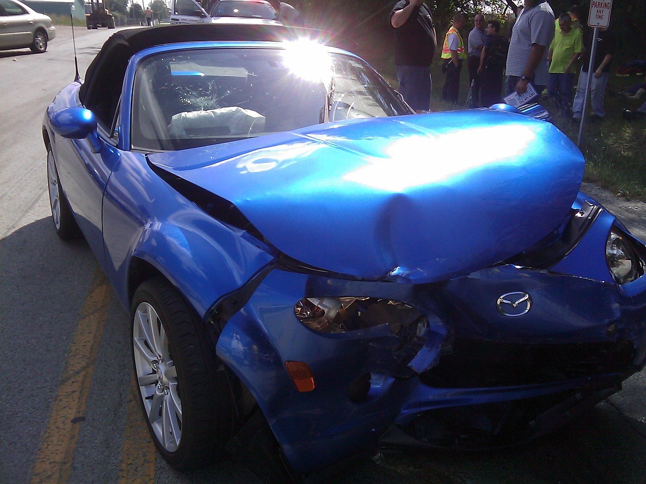 A blue convertible car with visible damage from a crash, showing dents and scratches on the bodywork