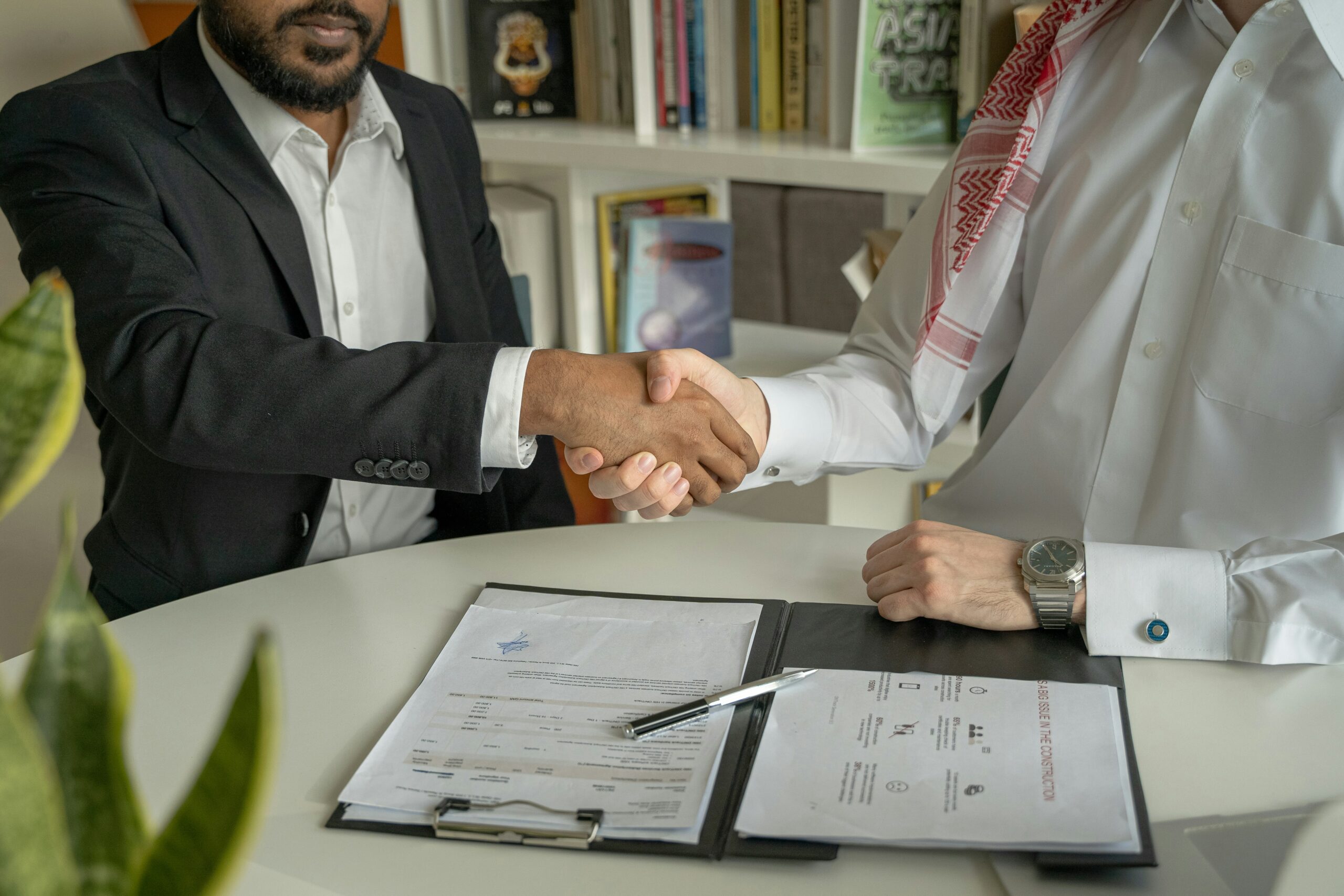 Two men shaking hands over a desk, symbolizing agreement or partnership in a professional setting.