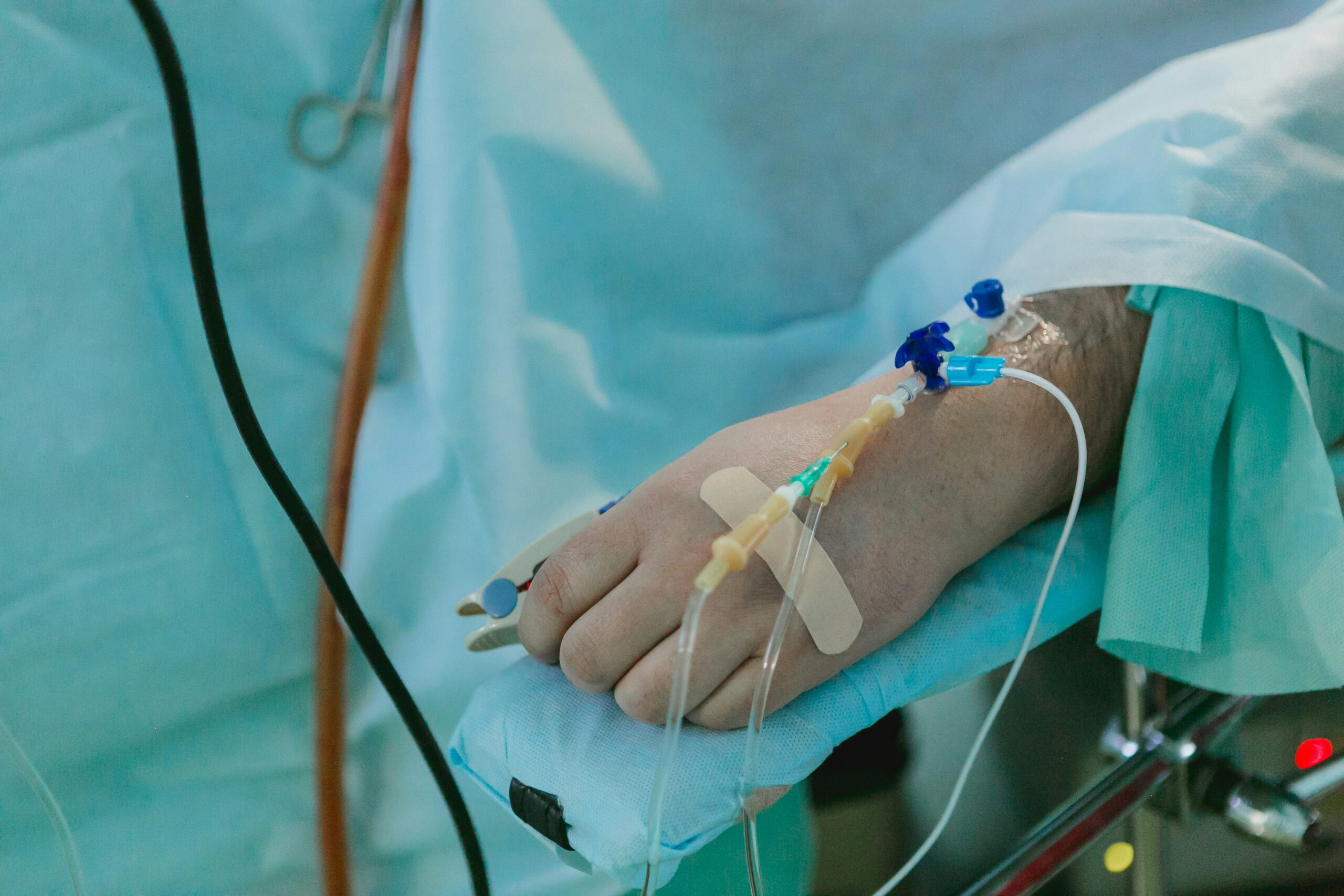a patient lies on a surgical bed. He is covered by a surgical curtain, but you can see the IV tubes in the top of his hand