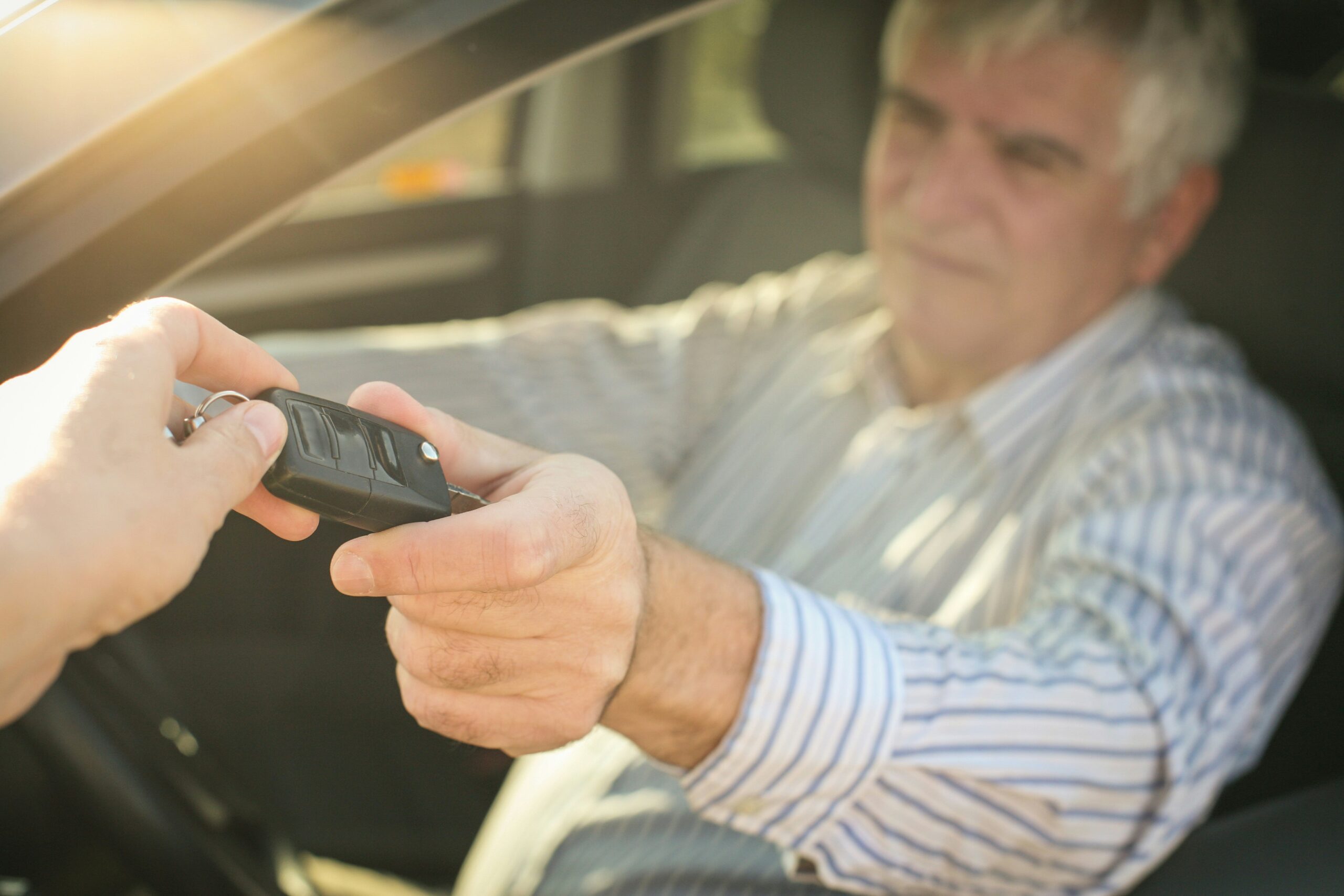 an older man hands his car keys out the window to someone else